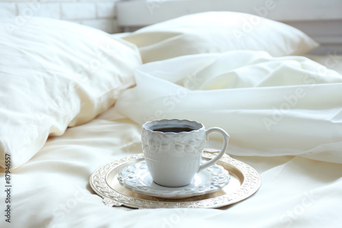 Morning cup of coffee on comfortable bed in bedroom