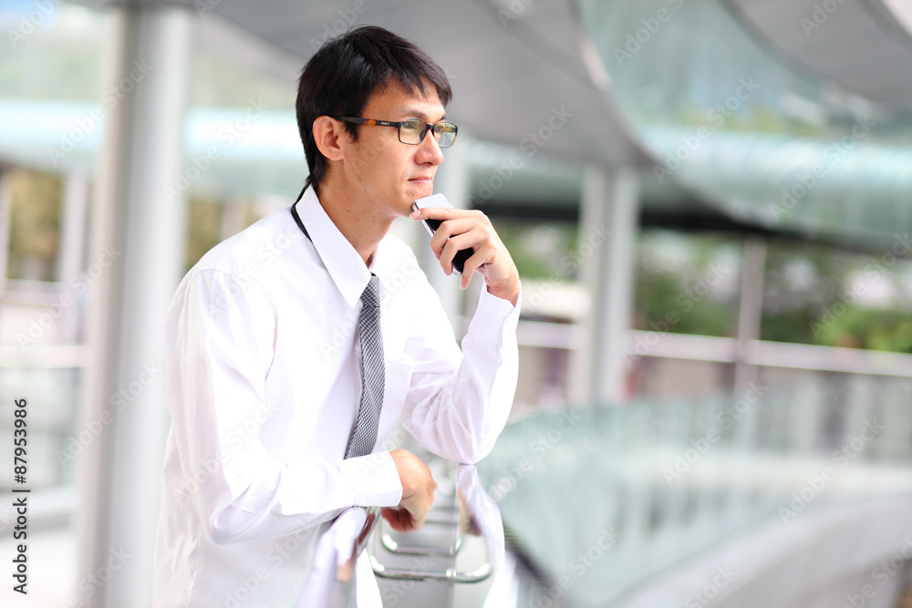 Portrait of young businessman thinking with smartphone.
