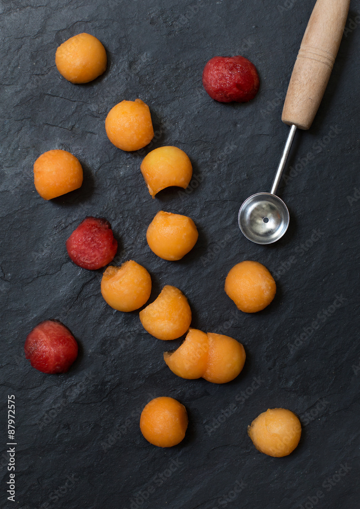 Melon balls with melon baller on stone background Melon balls with melon baller on stone background
