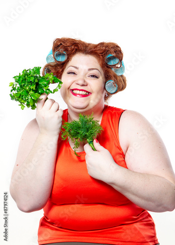 the fat woman wit red lipstick in curlers on a diet holding parsley and dill to eat isolated on the white background
