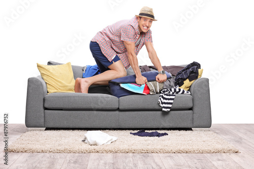 Young man packing a lot of clothes into one suitcase photo