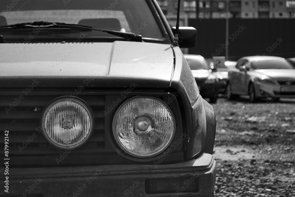 Close up on the vintage car. Composition of the front part of the vehicle with round light. Monochrome.