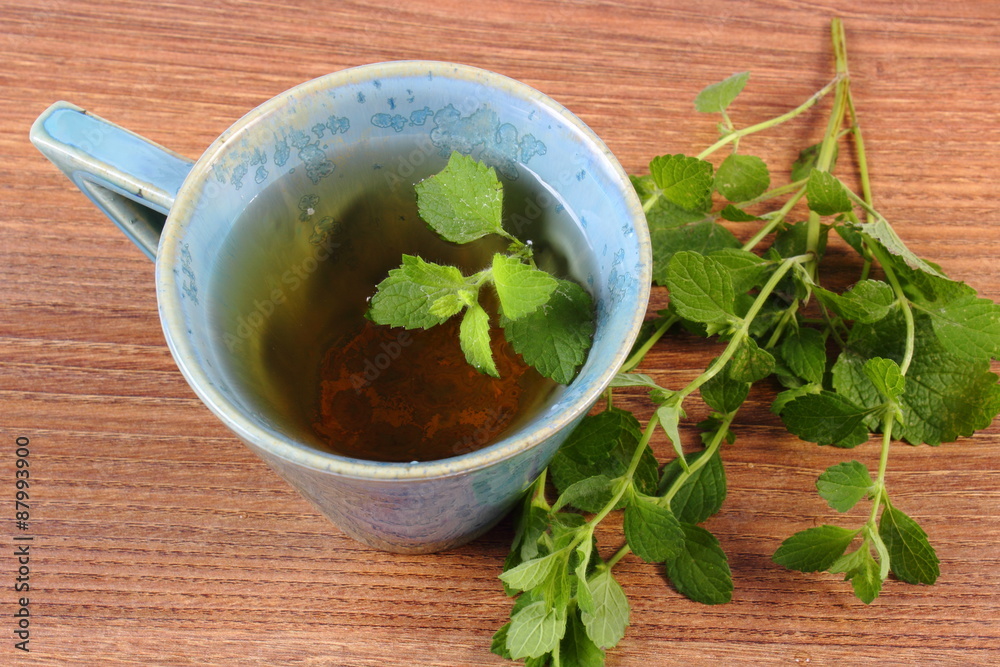Fresh lemon balm and cup of herbal drink on wooden table Fresh lemon balm and cup of herbal drink on wooden table