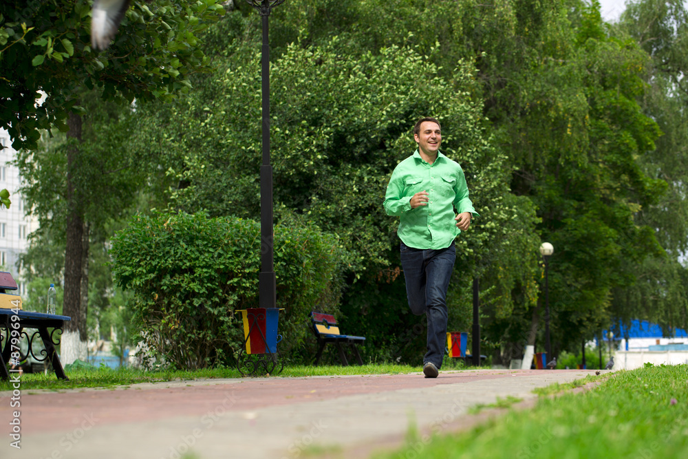 Young man in a green shirt and blue jeans running on summer park Young man in a green shirt and blue jeans running on summer park