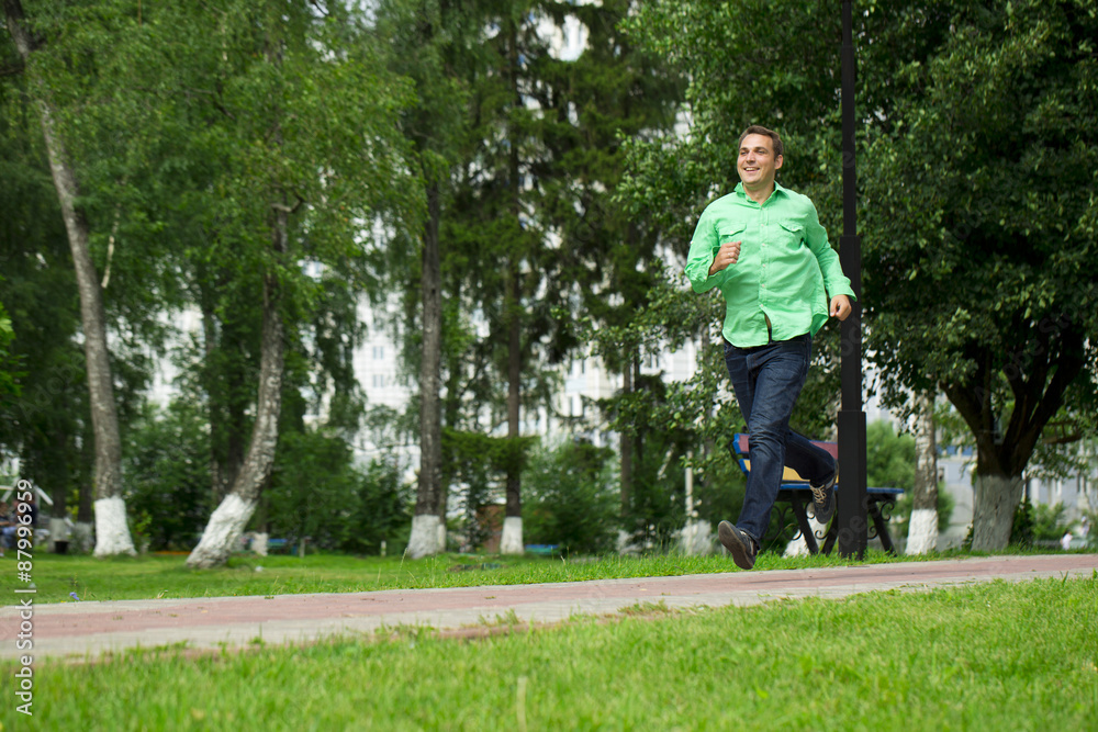 Young man in a green shirt and blue jeans running on summer park Young man in a green shirt and blue jeans running on summer park