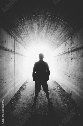 Young man stands in dark tunnel and looks in the glowing end, bl