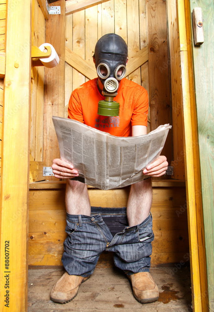 Φωτογραφία Man in respirator reading newspaper in wooden village WC