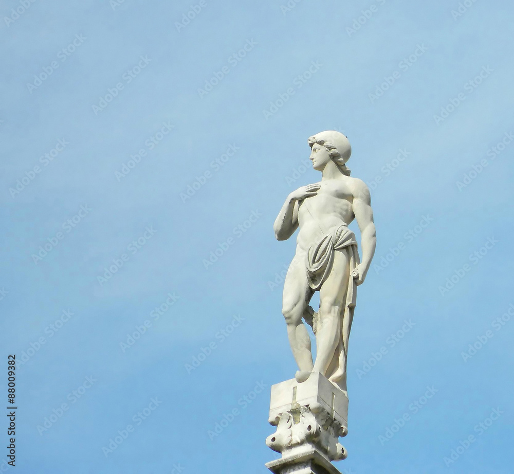 Statue on top of Milan Duomo roof spire with blue sky background