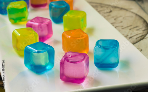 horizontal image of colourful plastic water filled ice cubes sitting on a white plate.
