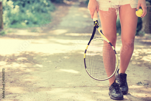 Cropped image legs of sportswoman with racket walking in park