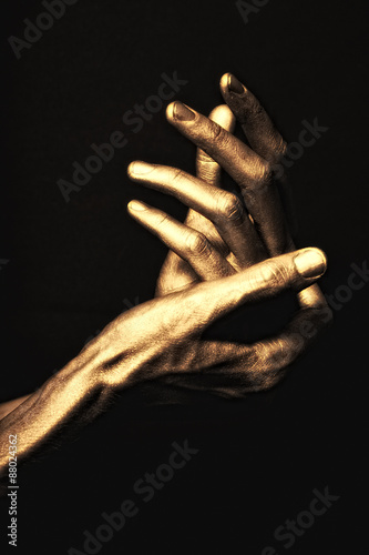 hands in golden paint on black background