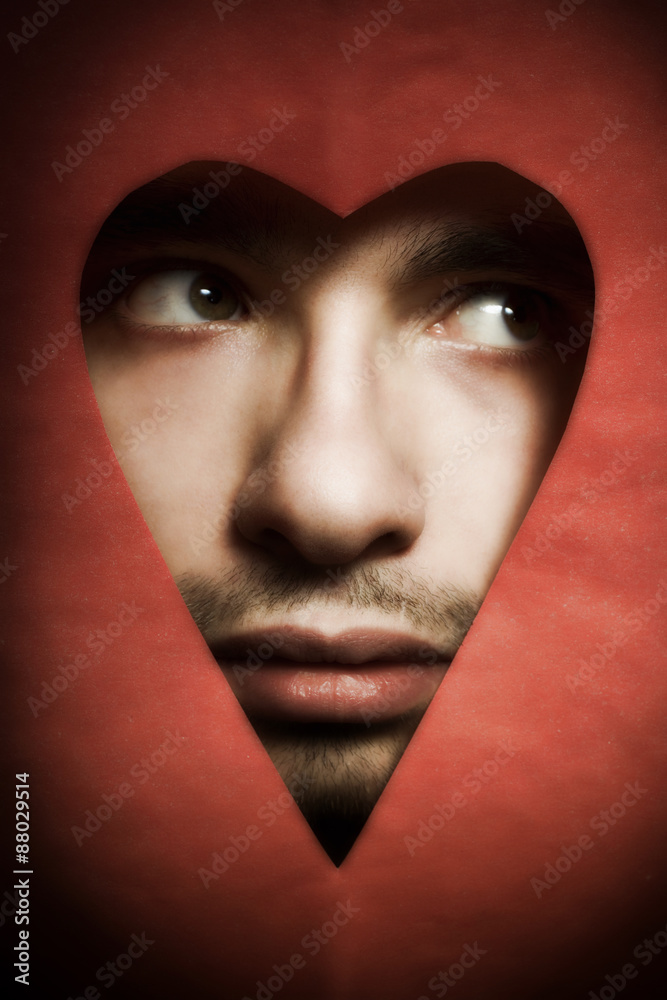 Face of young man peering from hole in heart-shaped