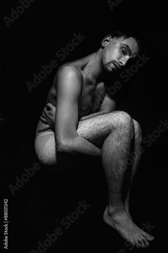 young naked man in his underwear lying on a black background