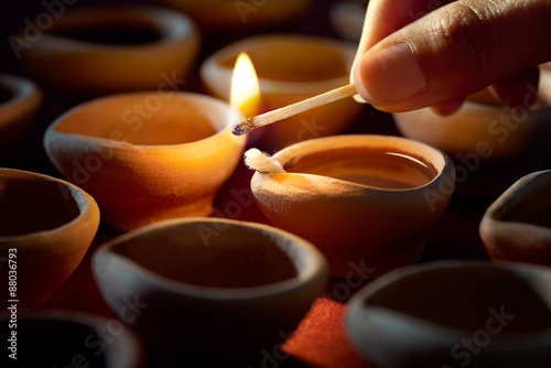 Hand holding a matchstick lighting diya lamps during diwali celebration