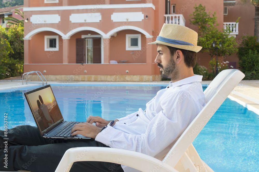 Young businessman looking picture on his laptop by the pool whil