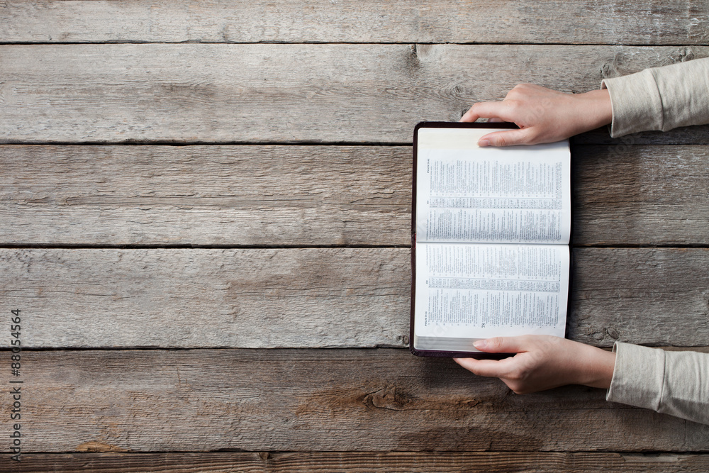 Obraz premium woman hands on bible. she is reading and praying over bible over wooden table