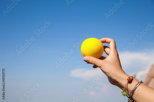 Girl hand holds a yellow ball in the sky background © sanchairat