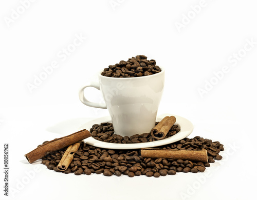 Coffee beans in a white coffee cup with four cinnamon stick on a