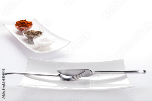 Salt, pepper, paprika in bowls in a row and a fork and a knife arranged on two plates