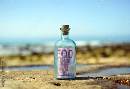Old glass bottle with 500 euro note inside on the rocks of the beach
