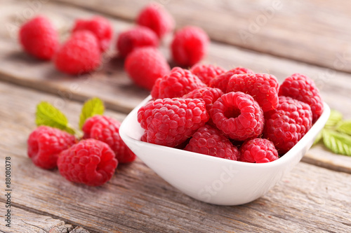 Red raspberries in bowl on grey wooden background