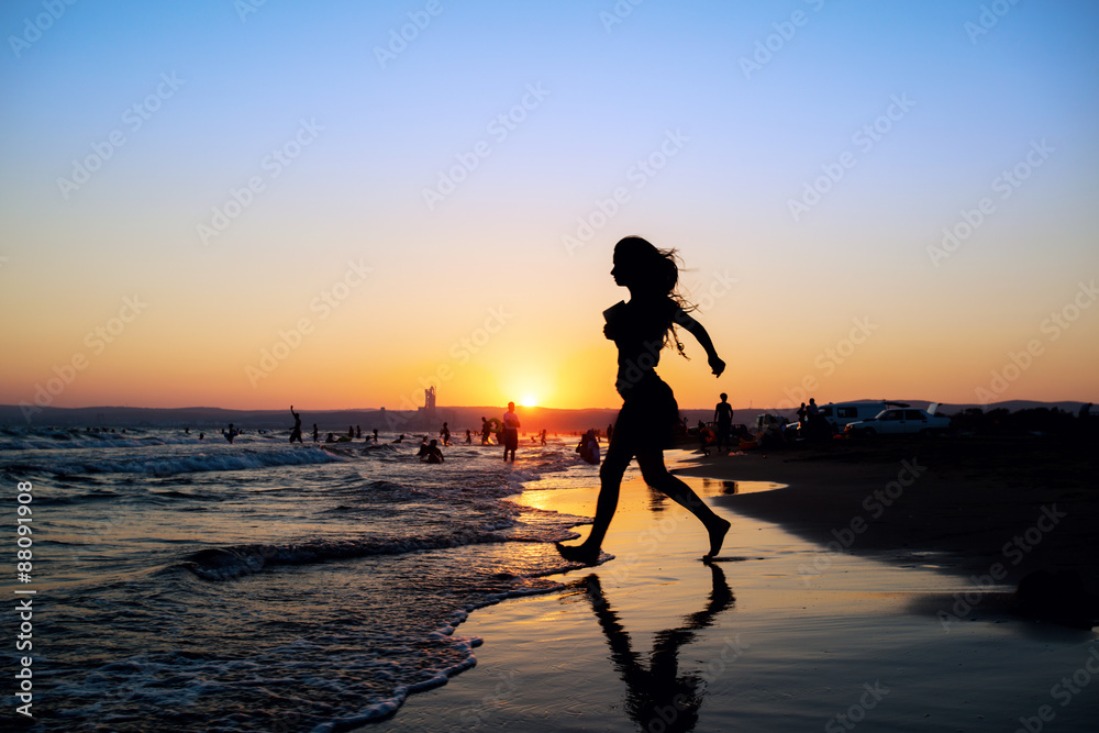 Woman at the beach running by the sea at sunset