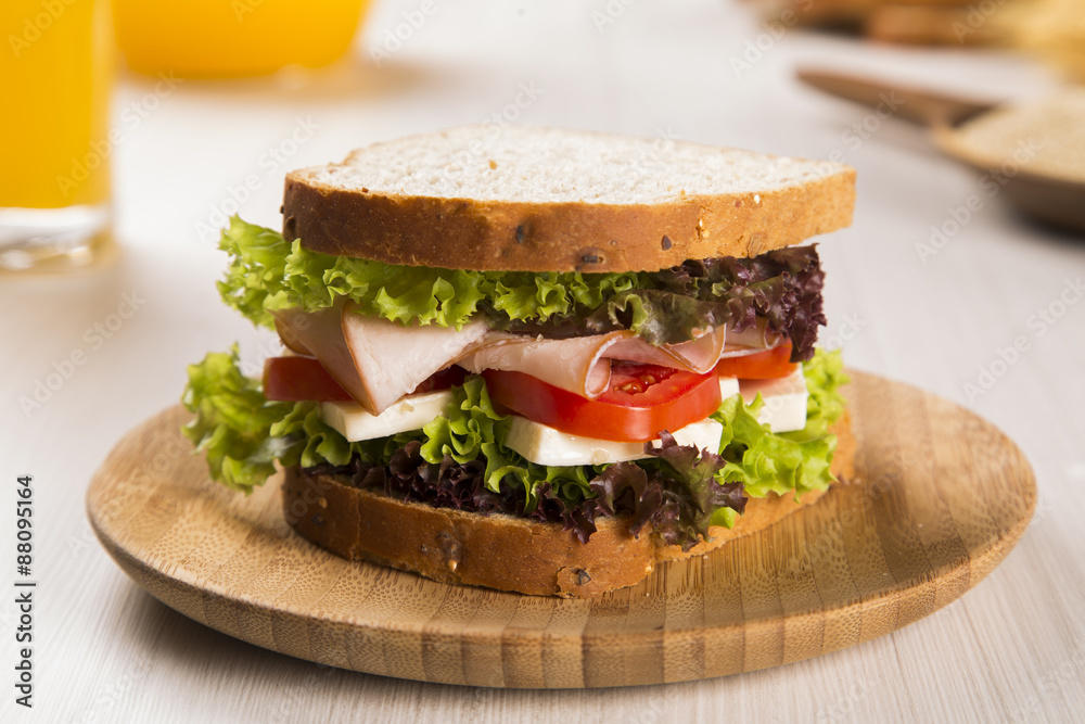 Sandwich on a white plate with turkey breast, tomato and lettuce.