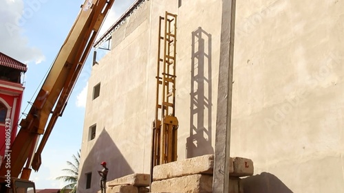 Large crane lifts a long concrete pile vertically and lowers it into place in a yellow steel pile driving frame / photo