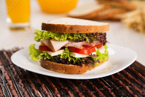 Sandwich on a white plate with turkey breast, tomato and lettuce.