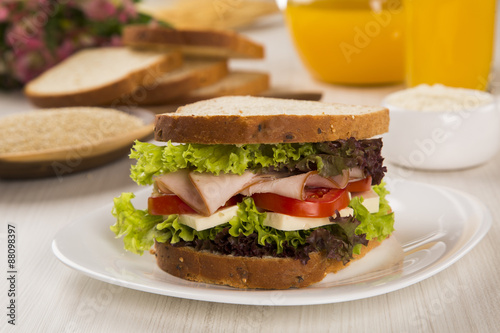 Sandwich on a white plate with turkey breast, tomato and lettuce.