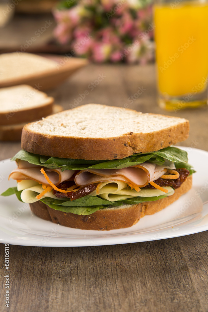Sandwich on a white plate with turkey breast, tomato and lettuce