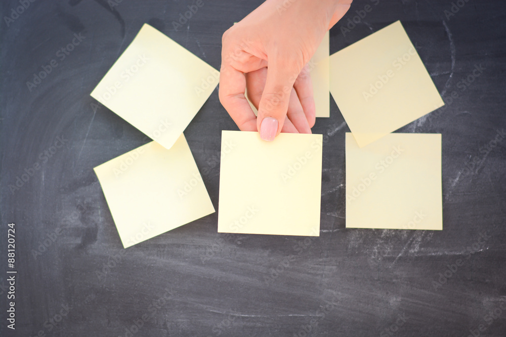 Woman hand posting empty adhesive notes on blackboard Woman hand posting empty adhesive notes on blackboard