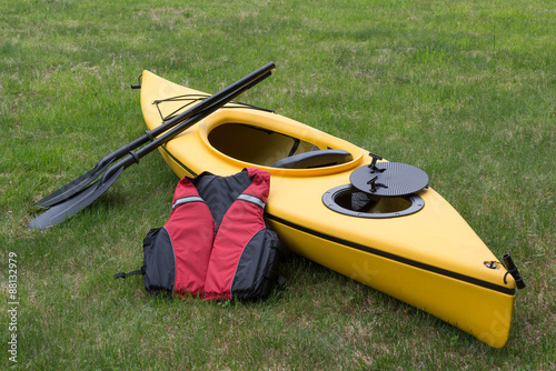 Yellow Kayak with Paddle and Life Vest on Green Grass. © Reid Dalland