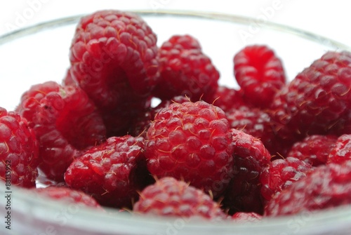 Ripe red juicy raspberries in a glass bowl on white background. Healthy/clean eating concept; fresh, organic, unprocessed food; paleo diet.