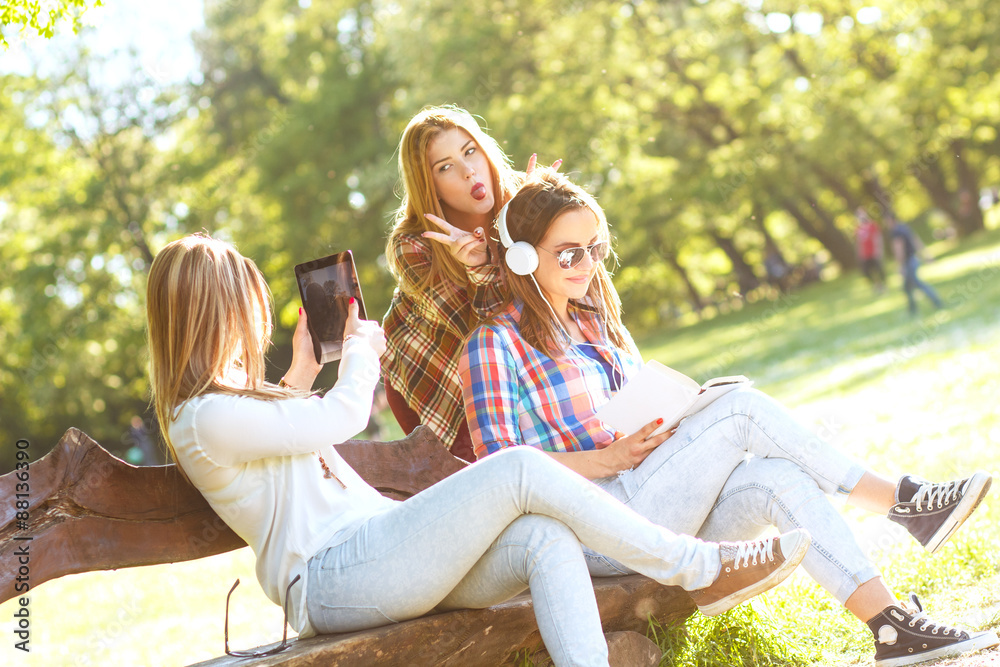 Three friends sitting in a park and looking something on tablet