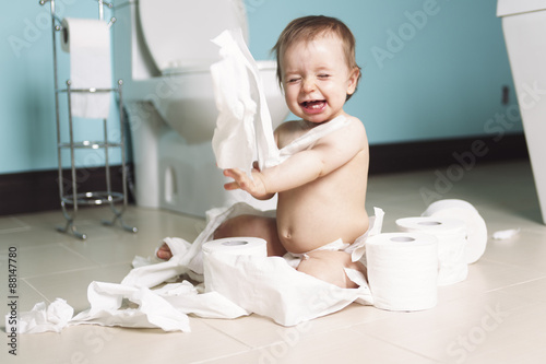 Toddler ripping up toilet paper in bathroom photo