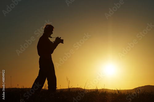 Silhouette of the photographer on a grassy horizon at sunset. Wooded mountains in the background.