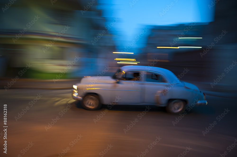 Vintage American car travels in motion blur through the dark streets of Havana at night
