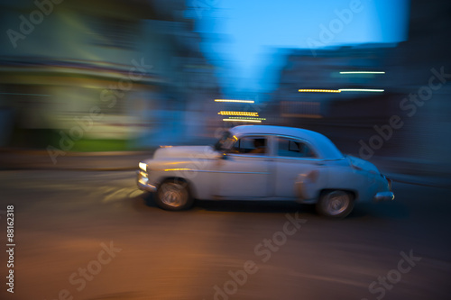 Vintage American car travels in motion blur through the dark streets of Havana at night