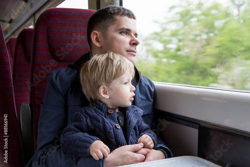 Young man - father, travelling with his little son by train, looking at the window.