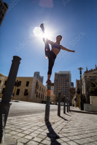 Athletic woman balancing on bollard and holding her leg