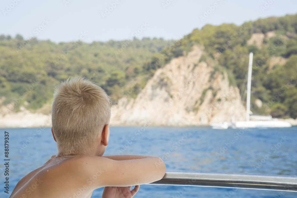 Fototapeta premium Boy looks at the boat in the sea and dreams