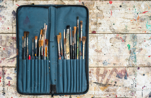 paint brushes in a open case on paint splatter wood background