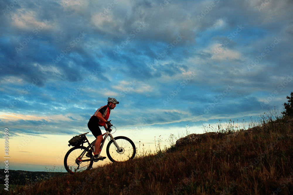 Silhouette of a biker and bicycle on sky background.