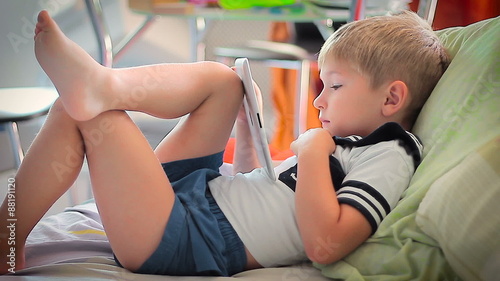 little boy watching tales on tablet on bed