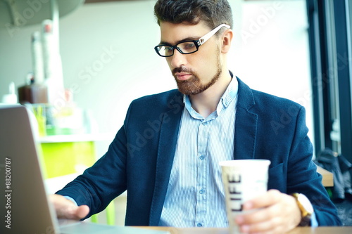 Young fashion smiling hipster man drinking coffee in the city cafe during lunch time with notebook in suit
