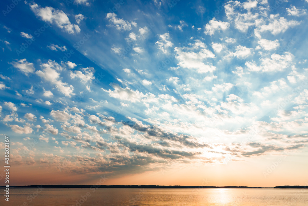 Obraz premium Clouds and sun rays over lake at sunrise