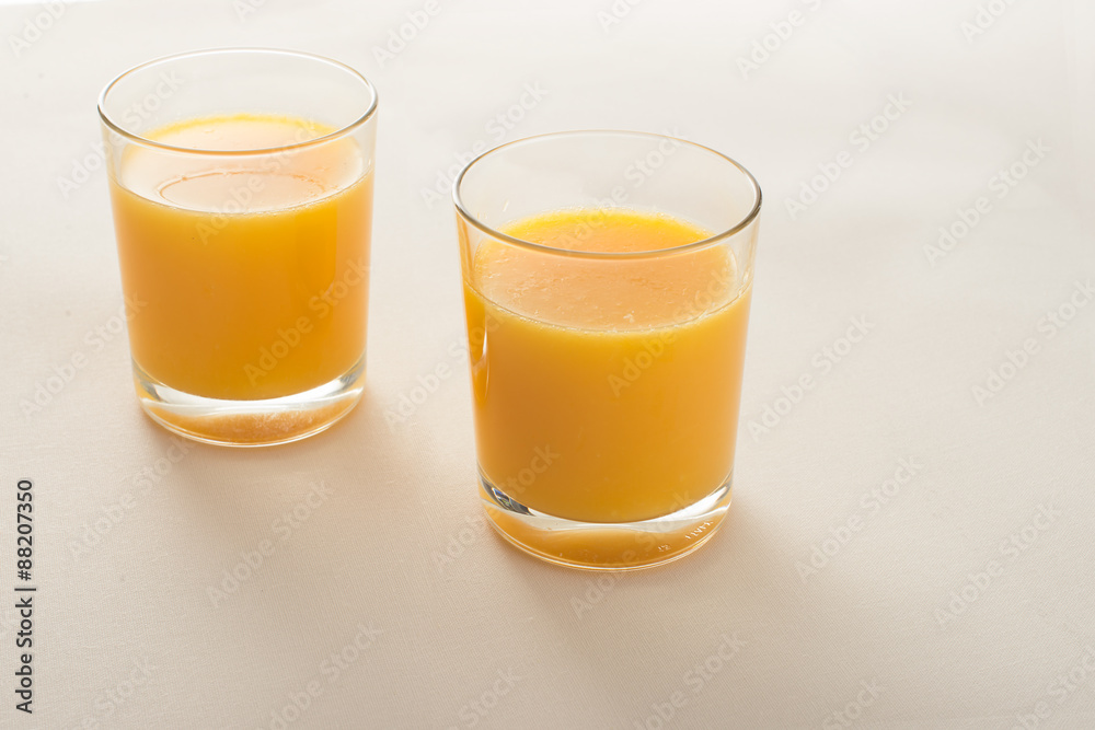 two glasses of orange juice on beige fabric background two glasses of orange juice on beige fabric background