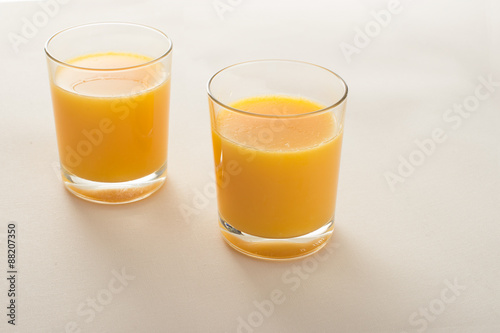 two glasses of orange juice on beige fabric background