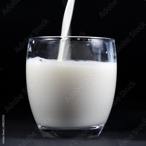 A stream of milk cow falls into a glass, on black background. Square image format